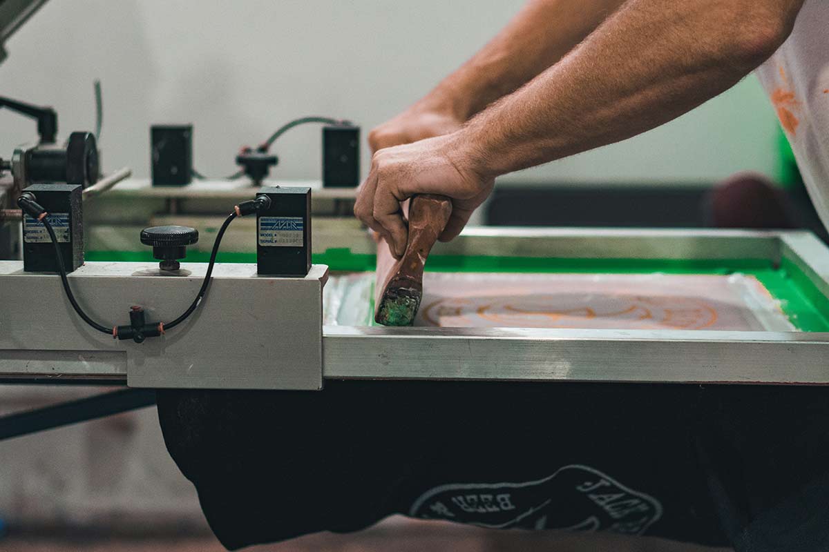 Person using a screen printing squeegee on a printing machine at Matchy factory
